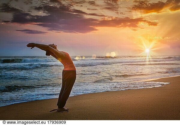 Junge sportlich fit Frau tun Yoga Sonnengruß Surya Namaskar Pose Hasta Uttanasana am tropischen Strand bei Sonnenuntergang. Mit Linsenreflexion