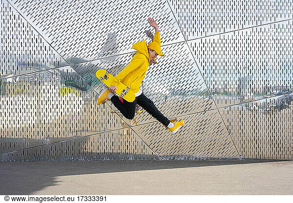 Junge springt  während er ein Skateboard an einer Metallwand hält
