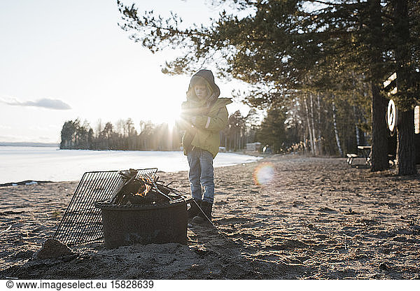 Junge stand neben einem Feuer am Strand in Schweden