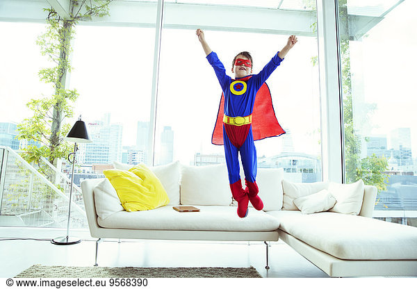 Junge Superheld springt vom Wohnzimmersofa