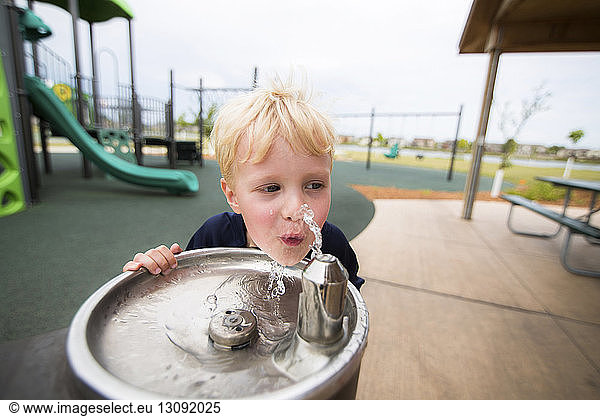 Junge trinkt Wasser auf dem Spielplatz