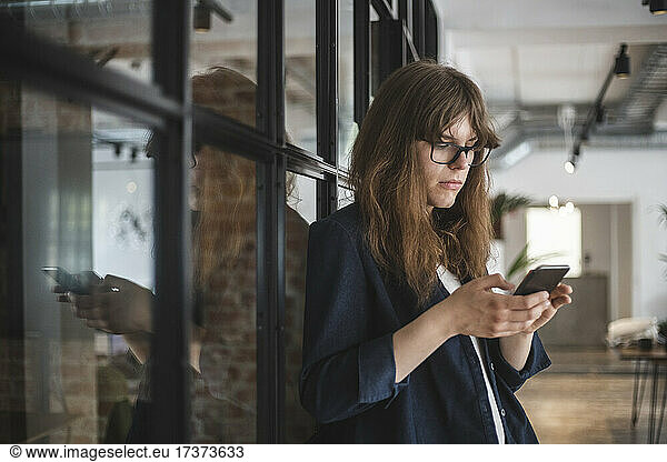 Junge Unternehmerin bei der Textnachrichtenübermittlung auf einem Smartphone in einem Start-up-Unternehmen
