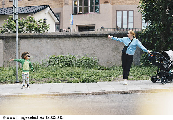 Junge zeigt und zeigt Mutter mit Kinderwagen beim Stehen auf dem Bürgersteig in der Stadt