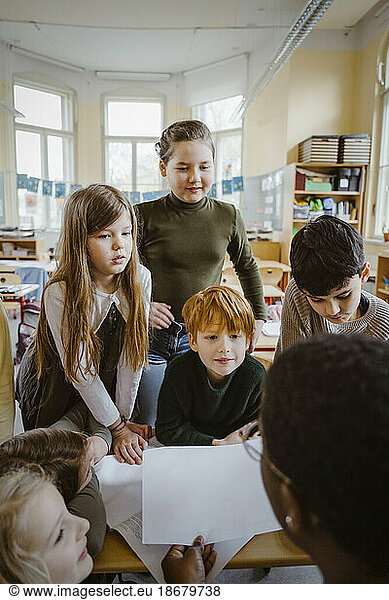 Jungen und Mädchen betrachten den Lehrer  der ihnen im Klassenzimmer hilft