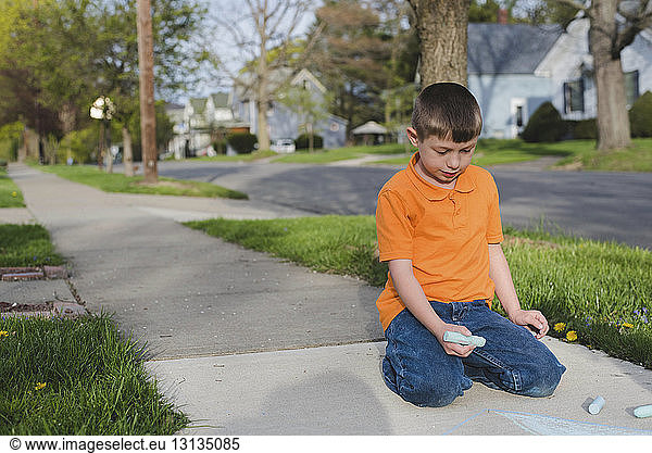 Jungenzeichnung mit Kreide auf Fußweg