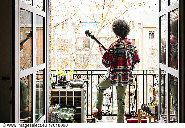 Junger Afroamerikaner übt Gitarre auf dem Balkon  gesehen durch eine Türöffnung