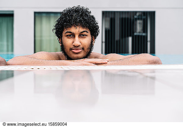 Junger Araber mit lockigem Haar  der sich am Rand eines Pools anlehnt