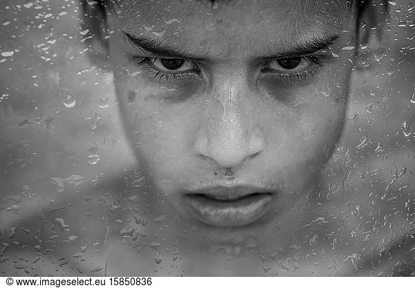 Junger brasilianischer Junge hinter dem mit Regentropfen bedeckten Fenster