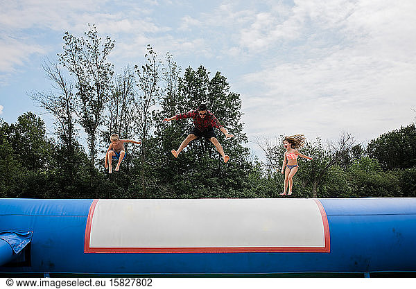 Junger Erwachsener und zwei Kinder springen an einem sonnigen Tag gegen den blauen Himmel