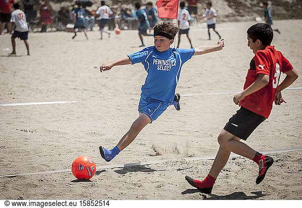 Junger Fussballspieler  der während eines Beach-Soccer-Spiels durch die Luft fliegt  um den Ball zu kicken