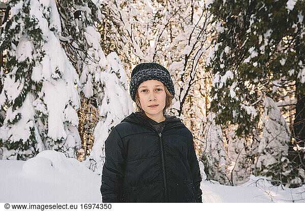 Junger Junge mit Mütze steht in einer verschneiten Szenerie.
