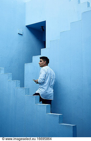 Junger lateinamerikanischer Mann hält sein Handy in einem blauen Gebäude