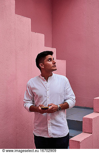 Junger lateinamerikanischer Mann hält sein Handy in einem rosa Gebäude