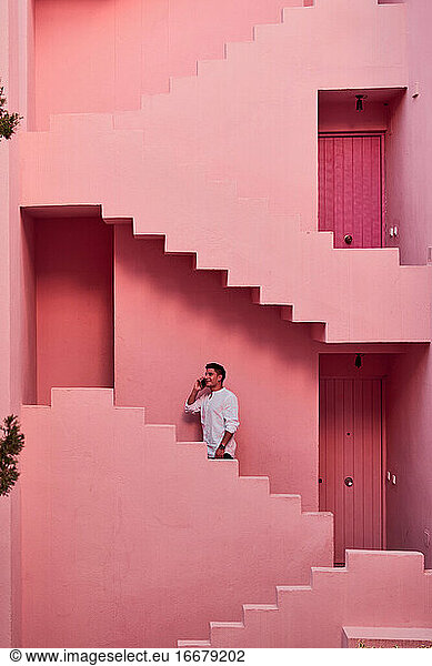 Junger lateinamerikanischer Mann spricht mit seinem Handy in einem rosa Gebäude