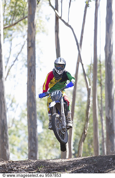 Junger männlicher Motocross-Fahrer beim Springen in der Luft im Wald