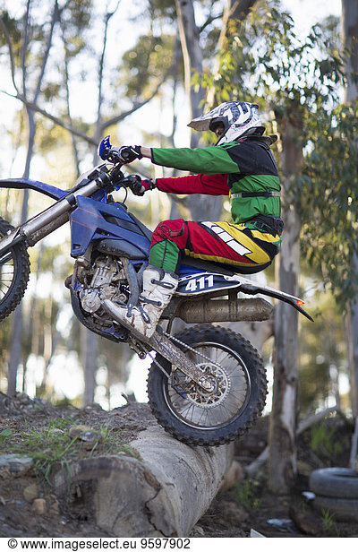 Junger männlicher Motocross-Rennfahrer  der über Baumstämme auf Waldwegen fährt