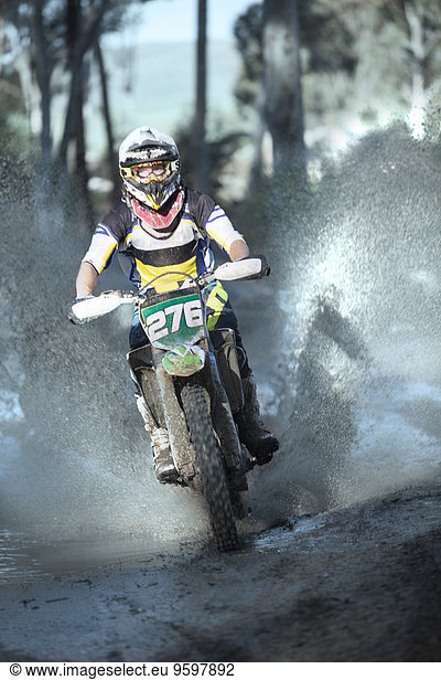 Junger  männlicher Motocross-Rennfahrer  der durch die Waldpfütze spritzt.