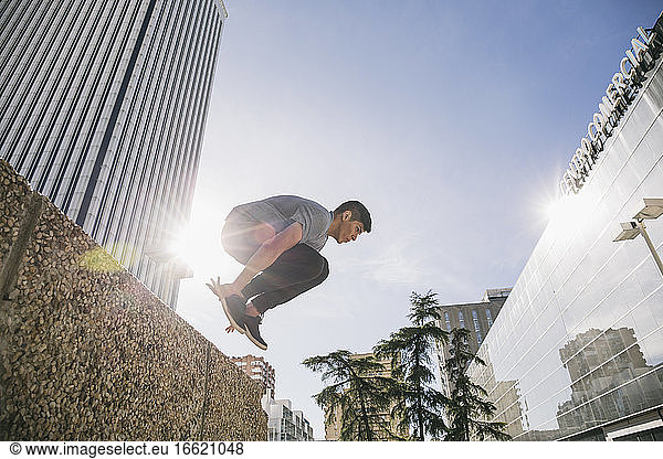 Junger Mann beim Parkour über die Stützmauer am Torre Picasso