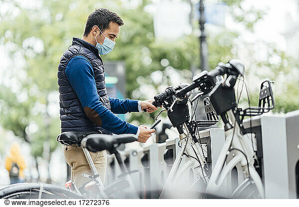 Junger Mann benutzt sein Smartphone an einem Fahrradparkplatz während des Coronavirus