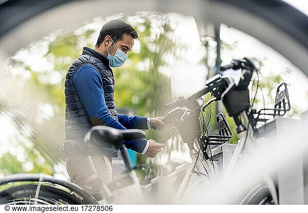 Junger Mann benutzt sein Smartphone an einer Fahrradparkstation während COVID-19