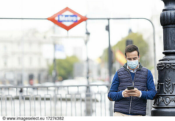 Junger Mann benutzt sein Smartphone und lehnt sich an einen Mast in der Stadt