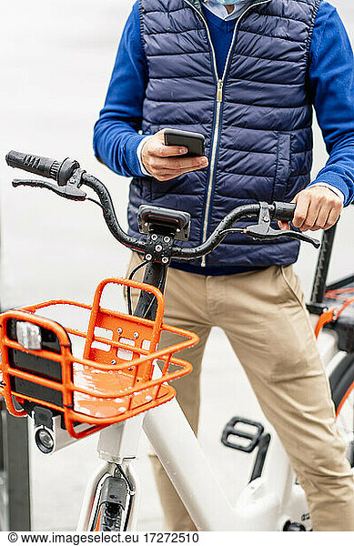 Junger Mann benutzt sein Smartphone  während er mit dem Fahrrad steht