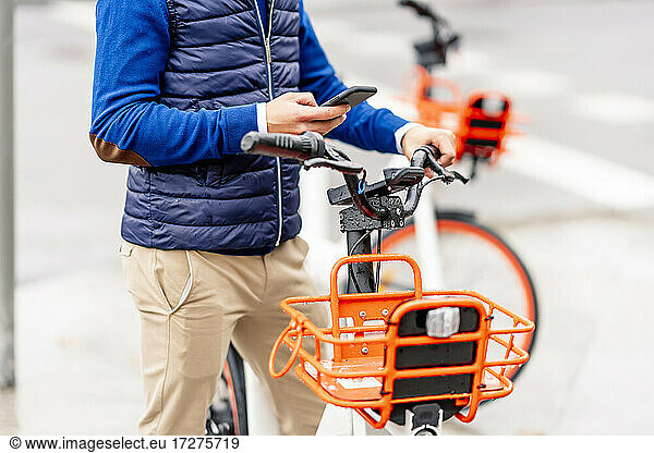 Junger Mann benutzt sein Smartphone  während er mit dem Fahrrad steht