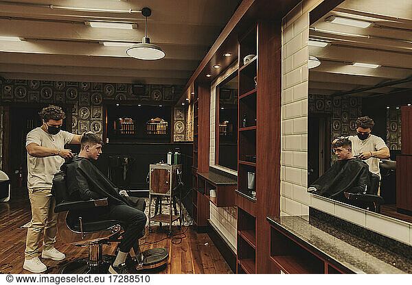 Junger Mann erhält einen Haarschnitt von einem männlichen Friseur in einem Salon während der COVID-19-Krise