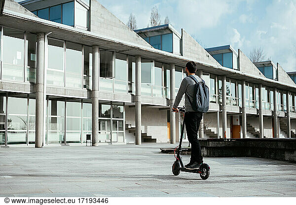 Junger Mann fährt Elektro-Scooter Fahrzeug außerhalb moderner Gebäude