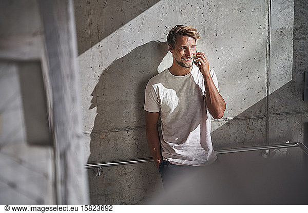 Junger Mann im T-Shirt telefoniert an Betonwand