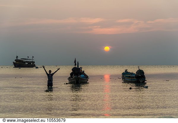 Junger Mann im Wasser mit zwei Longtail Booten  Südchinesisches Meer bei Sonnenuntergang  Golf von Thailand  Insel Koh Tao  Thailand  Asien