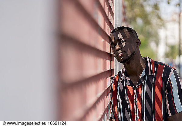 Junger Mann in Freizeitkleidung lehnt sich an einen Zaun im Freien