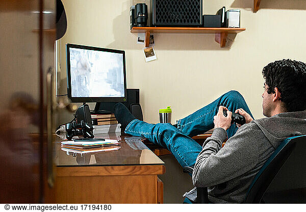 Junger Mann in Sweatshirt und Jeans  der in seinem Schlafzimmer Videospiele spielt.