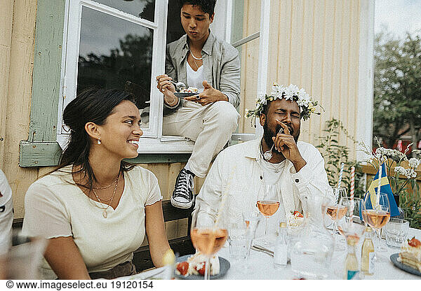 Junger Mann lacht beim Essen von Kuchen mit Freunden während einer Dinnerparty im Café