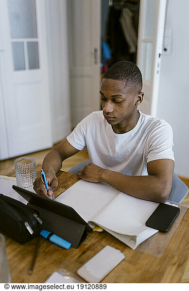 Junger Mann lernt mit digitalem Tablet zu Hause