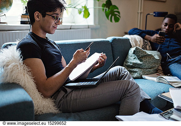 Junger Mann lernt  während ein Freund soziale Medien auf dem Sofa zu Hause nutzt