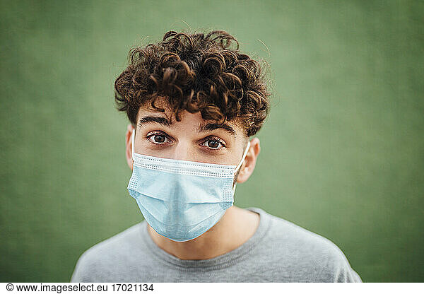 Junger Mann mit chirurgischer Maske vor grünem Hintergrund