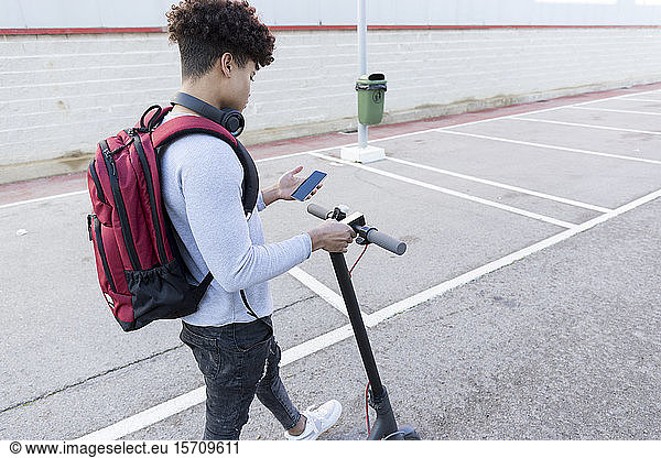 Junger Mann mit E-Scooter mit Smartphone