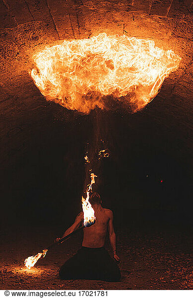 Junger Mann mit Feuerstab jongliert in dunklem Tunnel