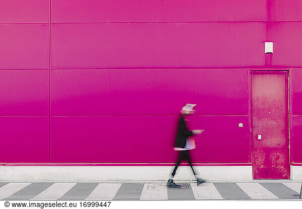 Junger Mann mit Kopfhörern  der an einer rosafarbenen Wand entlanggeht  unscharf