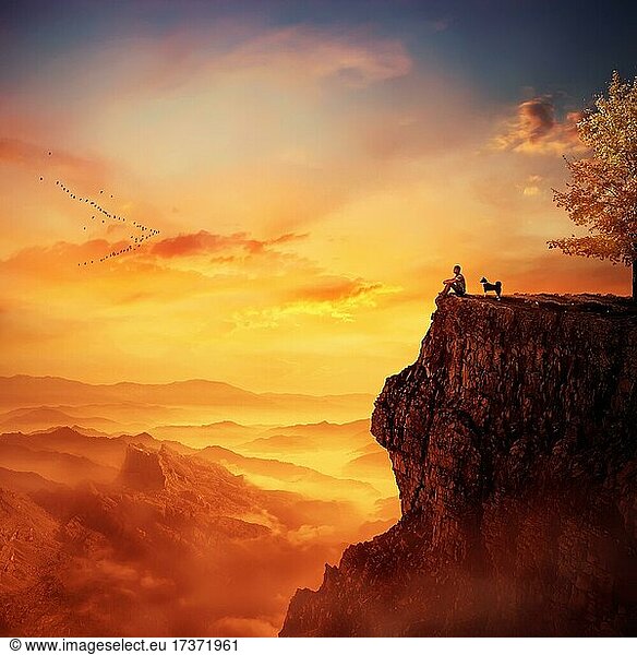 Junger Mann mit seinem treuen Hund  der auf dem Gipfel einer Klippe steht und den Sonnenuntergang über dem Tal beobachtet. Erinnerungen an die Kindheit  Freundschaft zwischen Mensch und Tier