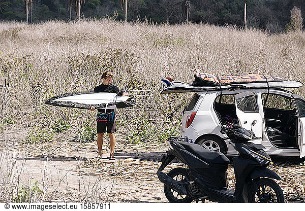 Junger Mann mit Surfbrett in der Nähe des Autos