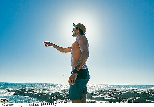 Junger Mann ohne Hemd  der auf den Ozean in Baja  Mexiko  zeigt.