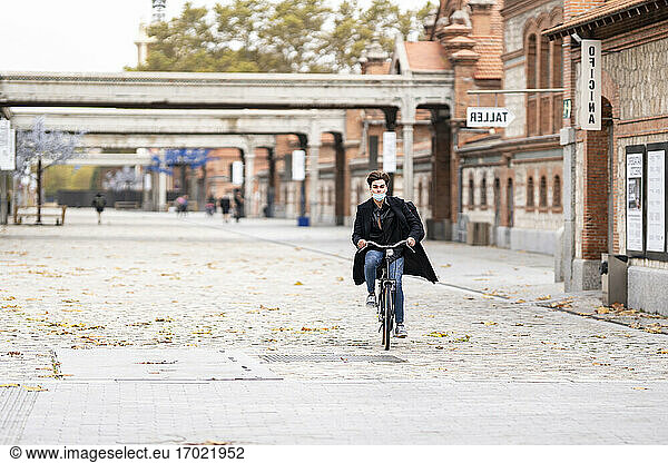 Junger Mann radelt auf der Straße mit Herbstblättern in der Stadt während der Pandemie
