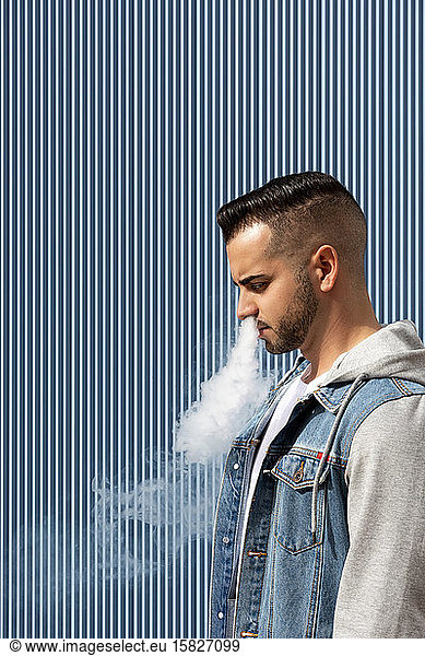 Junger Mann raucht mit einer elektronischen Zigarette auf blauem Hintergrund