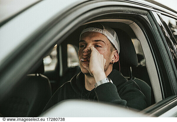 Junger Mann raucht Zigarette beim Autofahren