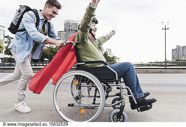 Junger Mann schiebt älteren Mann  der als Superheld verkleidet in einem Rollstuhl sitzt