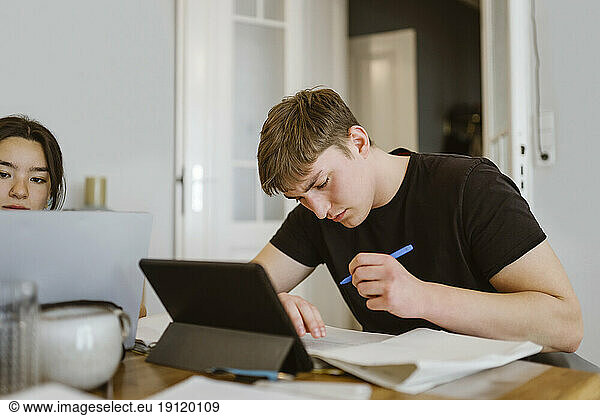 Junger Mann schreibt bei den Hausaufgaben bei einem Freund zu Hause