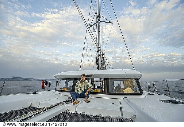 Junger Mann sitzt an Deck eines Segel-Katamaran  Segeltörn  Rhodos  Dodekanes