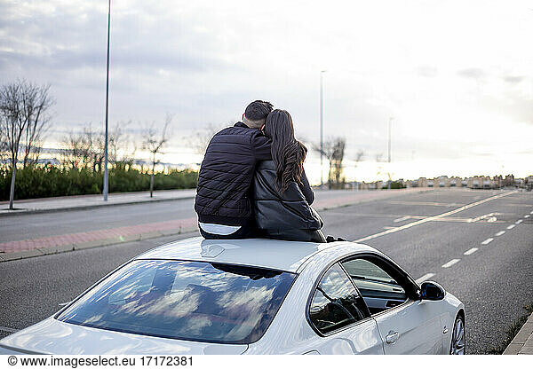 Junger Mann sitzt mit Frau auf dem Autodach